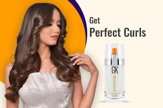 A model with long, wavy hair showcases GK Hair leave-in spray, promoting perfect curls against a vibrant orange background.